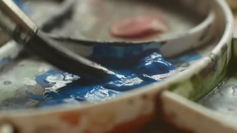 Dipping-paint-brush-into-blue-paint-on-artist-painting-palette,-close-up