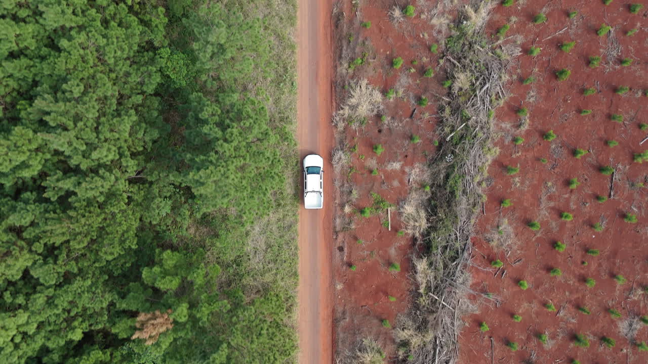 A car driving on a dirt road surrounded by forest and cleared land, aerial view