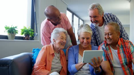 happy senior friends using digital tablet on sofa