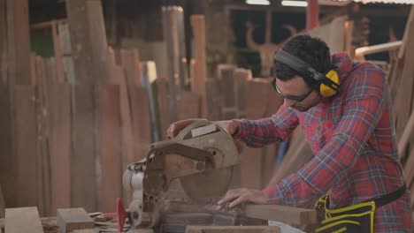 hombre carpintero guapo que usa gafas y tapones para la seguridad personal usando madera cortada por sierra circular para muebles en el lugar de trabajo de la fábrica.