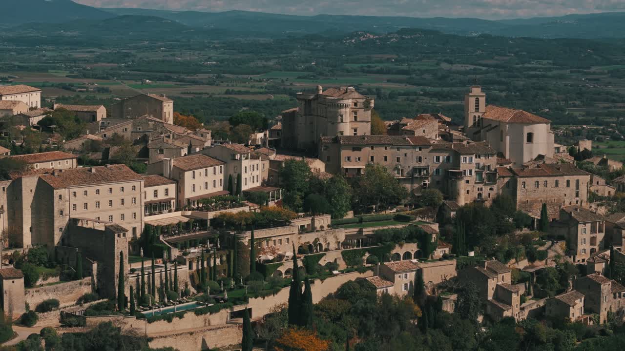 Aerial tracking right of Gordes, France, highlighting groves, vineyards, and autumn charm