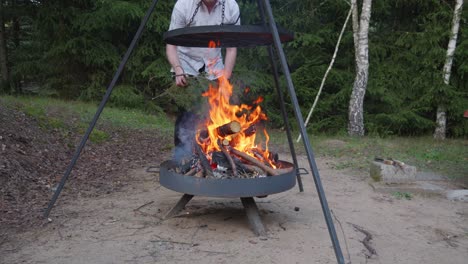 hombre de camisa blanca poniendo algunos bosques en la parrilla de la fogata o la parrilla del pozo de fuego con leña ardiendo en la chimenea