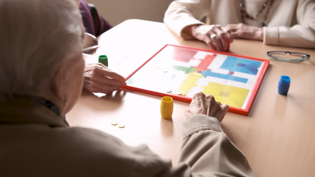 Senior friends playing ludo board game in nursing home