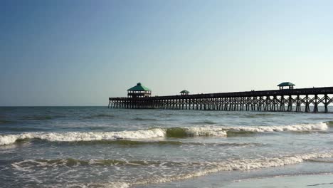 waves crash on the shore at folly beach pier on a hot summer day, south carolina