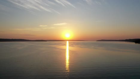 panning aerial view across a glassy lake during golden hour with the sun reflection off the lake