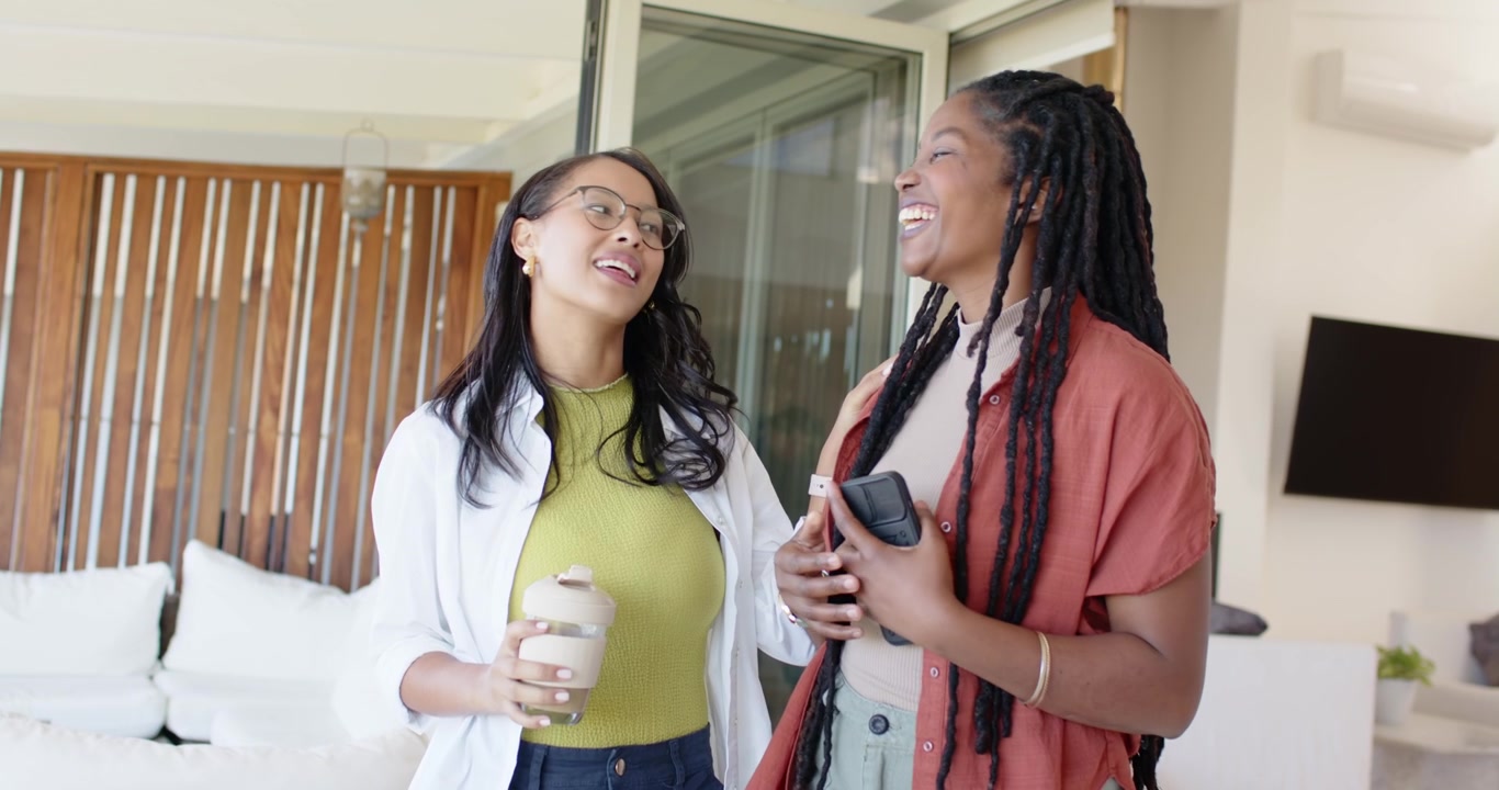 African American friends starting chat on covered patio, holding mug and phone, reacting outside