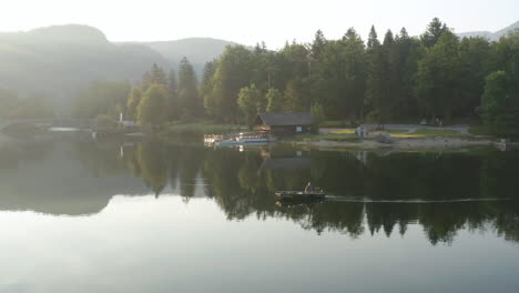 fisherman on boat floating at lake bohinj on bright sunny day with reflections on tranquil water