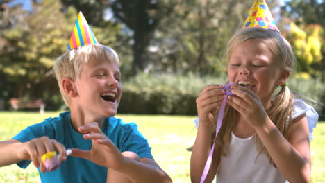 brother playing with party horn next to his sister