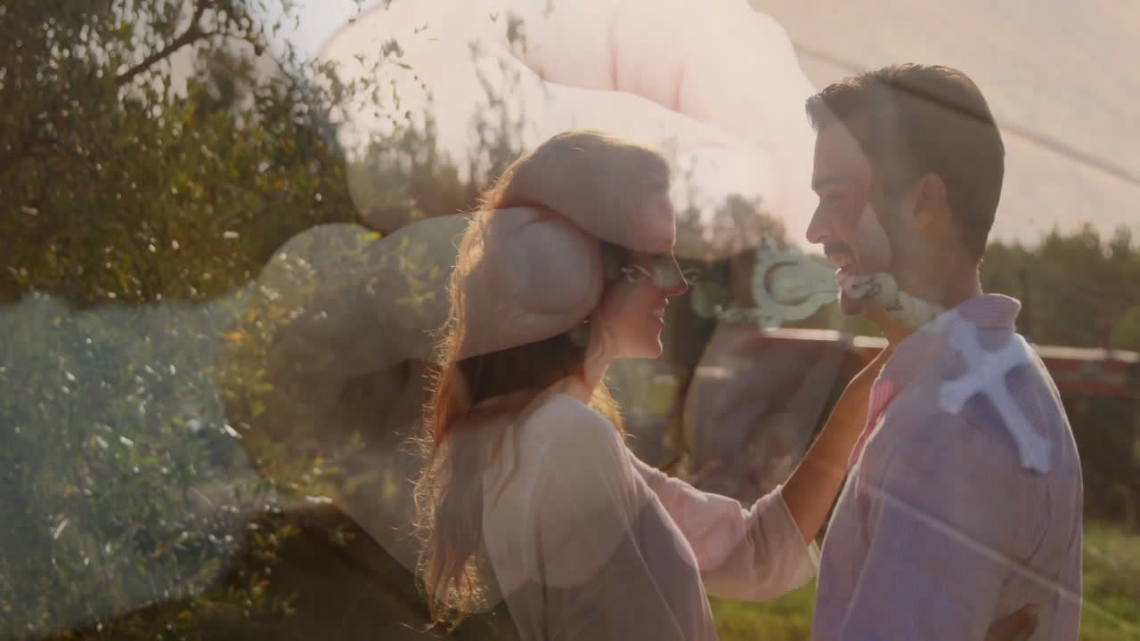 Couple sharing affectionate gaze in sunlit field, showing animated rosary cross overlay for health