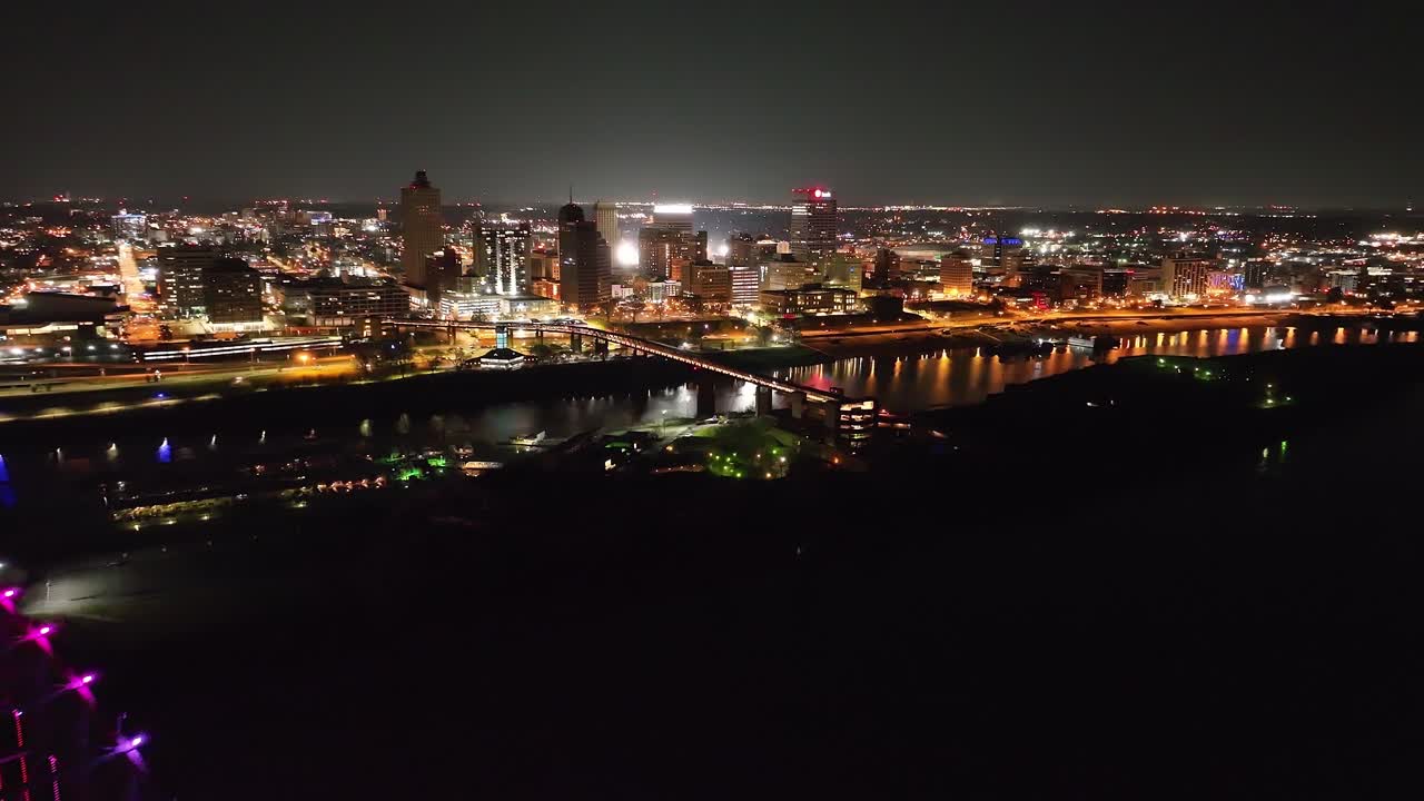 Memphis, Tennessee skyline with Mississippi River pulling back to Hernado De Soto bridge with drone video at night