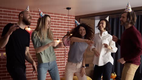 Joyful-friends-in-hats-dancing-on-birthday-party-celebrating-holiday-at-home,-slowmo