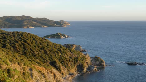 Slot-motion-shot-of-idyllic-hilly-Mediterranean-coastline-with-vegetation-in-golden-afternoon-sun-and-blue-water-in-Chia,-Southern-Sardinia,-Italy