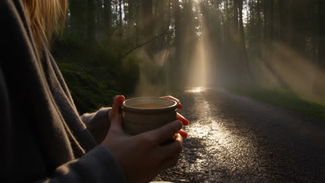 person holding a steaming mug in a sunlit forest