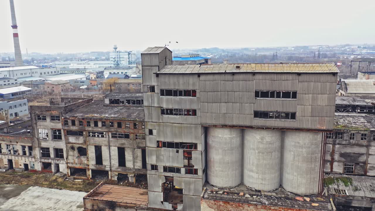 A huge state-owned factory with gray walls and broken glasses in the windows on the background of city buildings. Industrial zone. Aerial view.