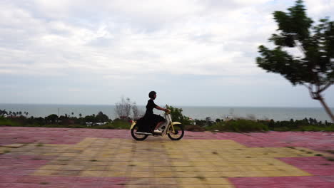 female in black dress riding vintage motorbike on coastline of vietnam, motion view