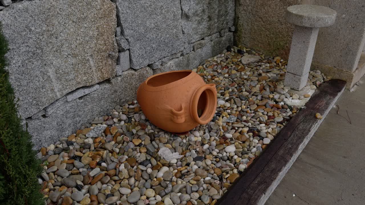 Beautiful Garden Vase Standing On Colourful Pebbles Next To A Stone Wall