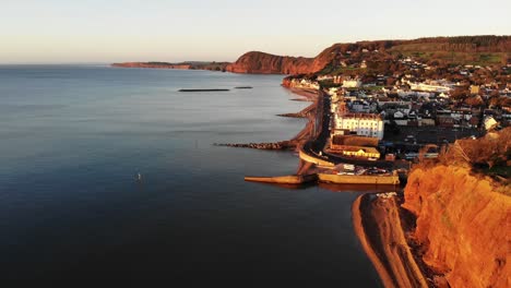 aerial hugging along coastline with sidmouth town bathed in golden sunrise light