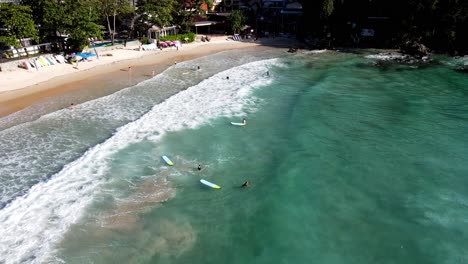 aerial flying over waves breaking on kata beach in phuket near resort bar