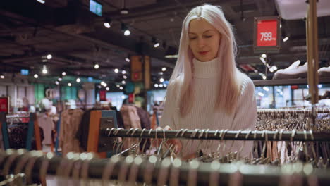calm focused lady browsing rack of pants selecting white pair with hanger running fingers over fabric assessing fit and quality in modern boutique setting with soft lighting and minimal decor