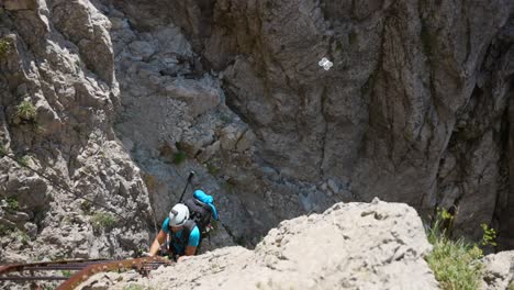 a climber ascends a rugged cliffside while a drone captures the action. the man is equipped with a helmet. extreme outdoor adventure in the mountains