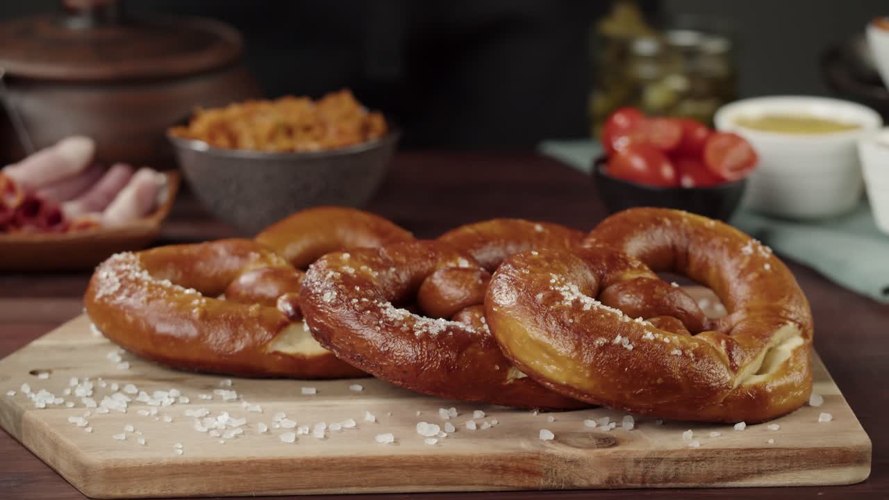 Hands Placing Freshly Baked Pretzels with Coarse Salt on a Wooden Board