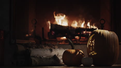 una gran calabaza luminosa yace en el crepúsculo junto a una chimenea encendida. la casa está decorada para halloween, las vacaciones de otoño