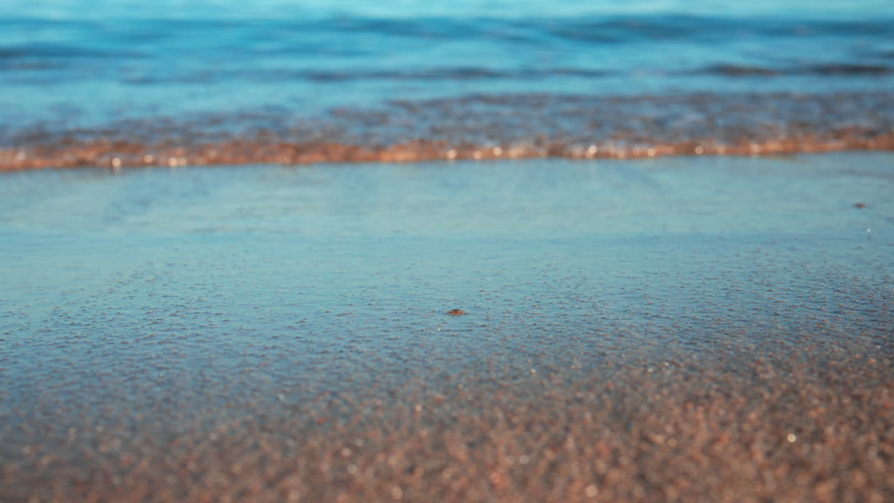 Close up of small waves rolling gently onto the sandy beach under morning light