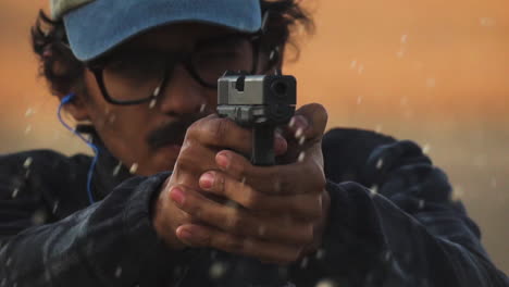 young american man firing gun at shooting range, wearing cap and ear protectors