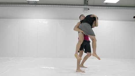 two male wrestlers in a white room work out throwing mats. take a grapple and throw through yourself.