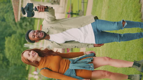 video vertical de una joven pareja viajando por la ciudad juntos vlogging a la cámara de video en el parque