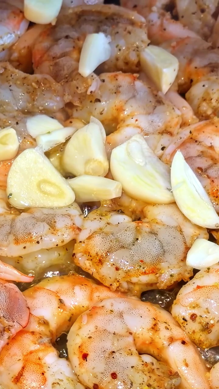 Shrimp seasoned and cooking in a hot pan with bubbling oil and sliced garlic cloves, showing gradual color change during frying. Vertical video