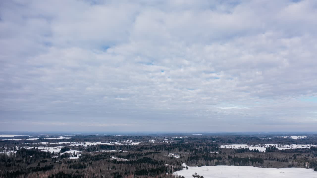Aerial cloud timelapse over the forest in snow covered winter day. Drone hyperlapse in overcast countryside landscape.