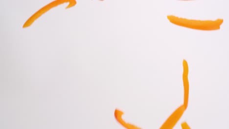 bright orange bell pepper julienned slices raining down on white backdrop in slow motion