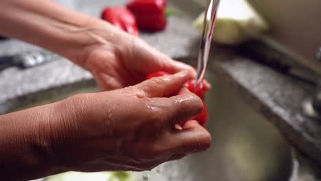 washing red bell pepper in running water at the kitchen sink