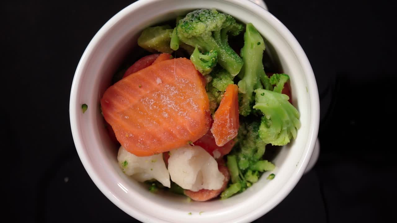 Rotating bowl filled with frozen mixed vegetables broccoli, carrots, and cauliflower. Healthy food concept, balanced diet, and frozen meal ingredients