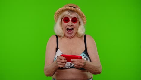 Senior-addicted-woman-tourist-in-red-sunglasses-enjoying-smartphone-gadget-video-games-on-chroma-key