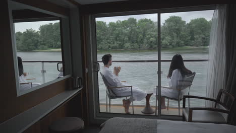 Young-couple-in-bathrobe-having-a-drink-on-cruise-ship-room-terrace