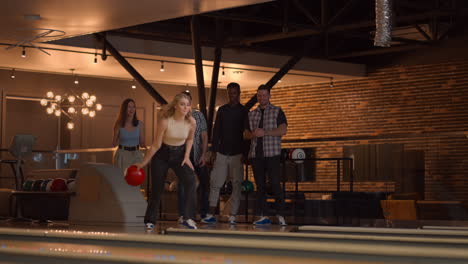 a beautiful blonde throws a bowling ball and knocks out a shot with one throw and hugs and rejoices with her friends. multi-ethnic group of friends bowling