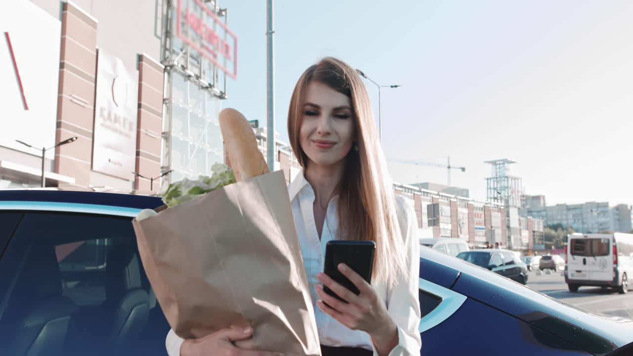 Woman with a mobile phone near recharging electric car vehicle charging at public charging station