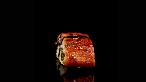 unagi sushi rotates smoothly on a reflective black surface, illuminated by studio lighting. camera remains static, emphasizing texture, color, and glossy presentation