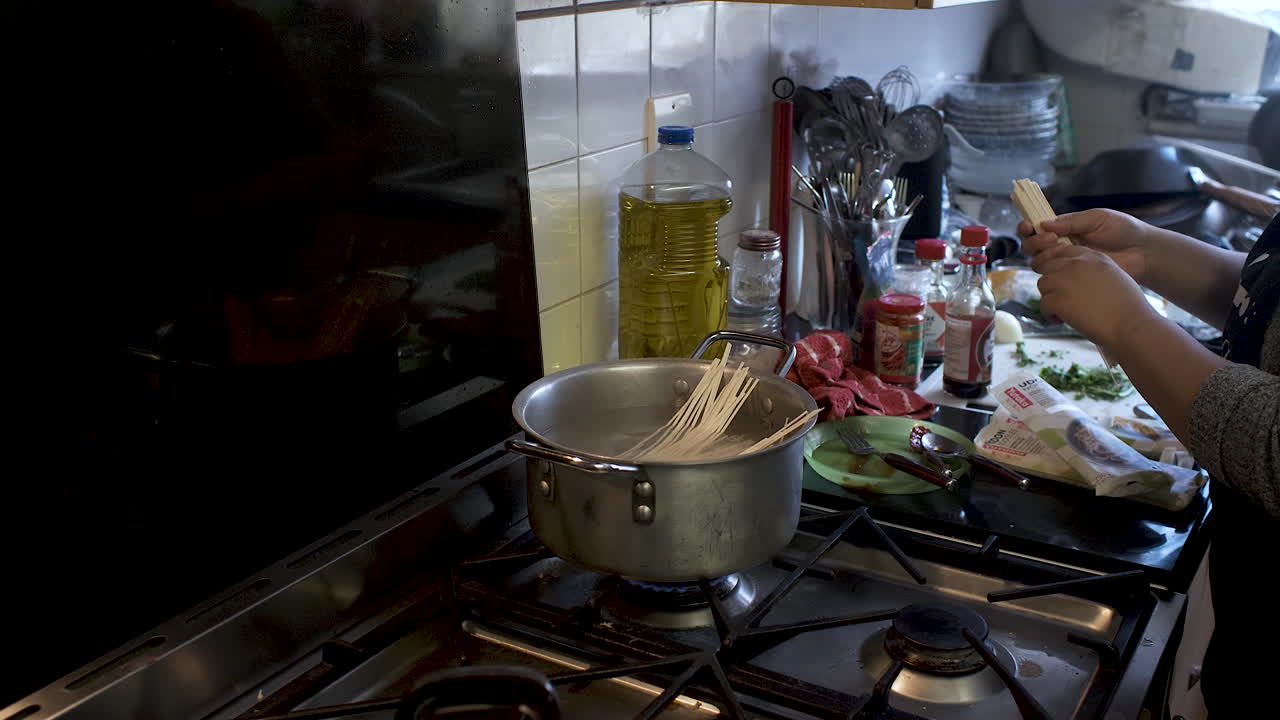 mano femenina colocando fideos de espagueti crudos en una olla grande con agua en la cocina dentro de la cocina