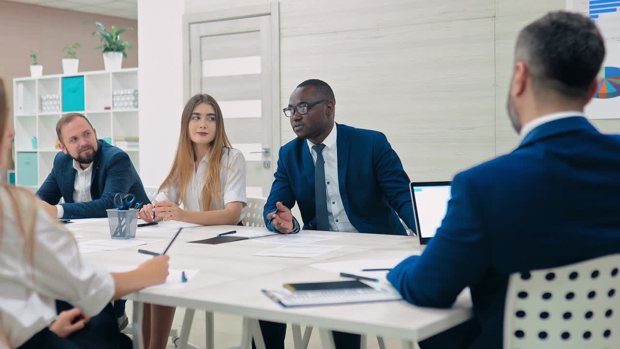 Dark-skinned businessman tells partners his business plan. Business meeting in a modern business center. International team of young businessmen.