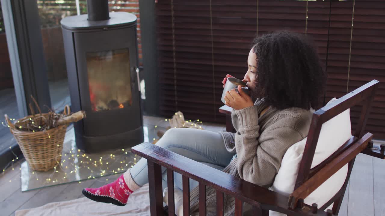 Donna afroamericana che beve caffè mentre è seduta vicino al caminetto nella casa vacanze.
