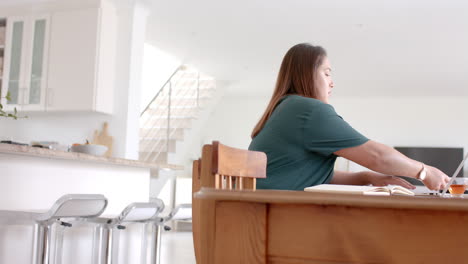 thoughtful plus size biracial woman drinking tea and using laptop at home, copy space, slow motion
