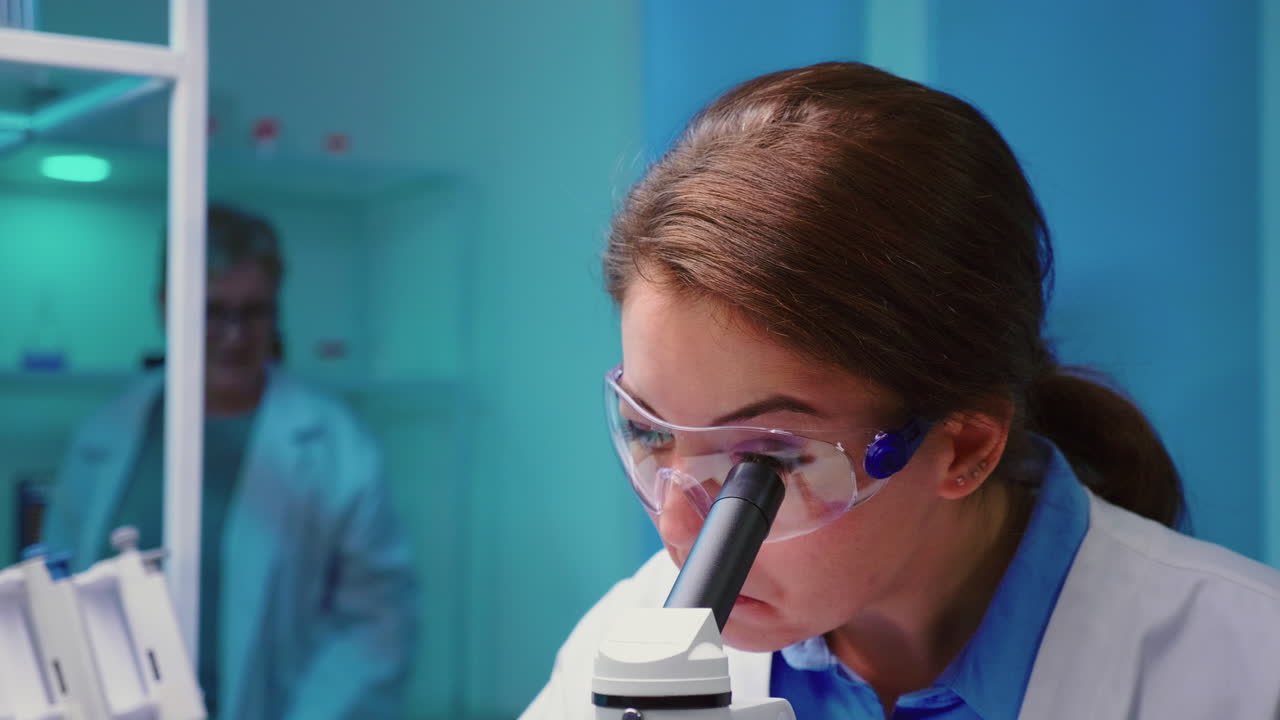 Primo piano di una dottoressa chimica che osserva attraverso un microscopio.