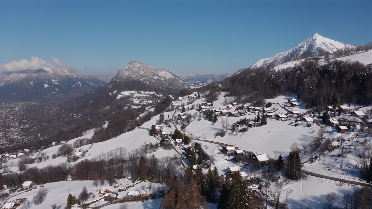 Lateral truck drone shot of snow covered village in Haute-Savoie, on a blue bird sunny day with Marcelly peak and Moll in the background.