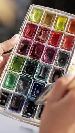 person painting with watercolor palette and brush