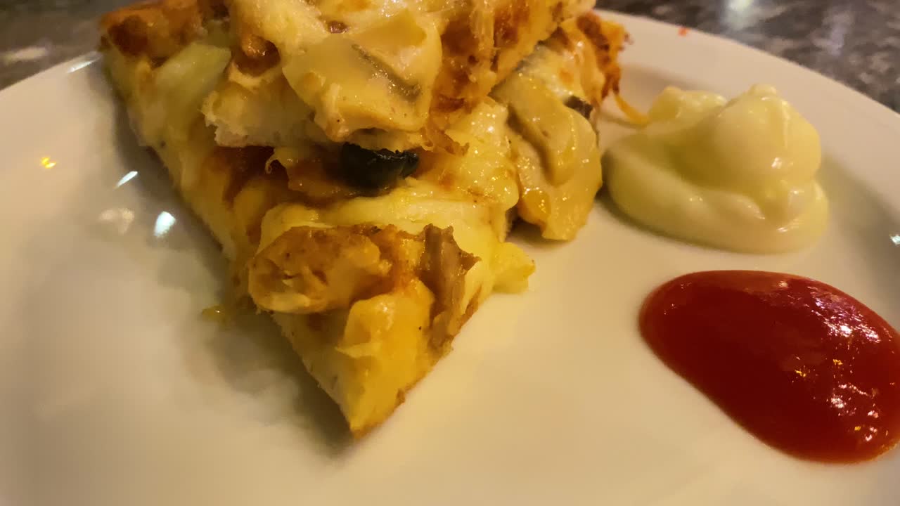 primer plano de una porción de pizza estilo americano con ketchup y mayonesa, de mano