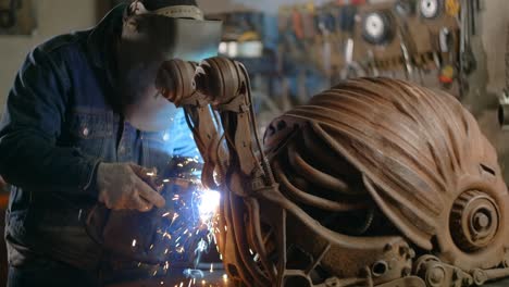 locksmith welds the decorative metal steampunk snail sculpture with a lot of sparks and flashes in slow motion, metalwork at workshop, 4k 60p prores hq