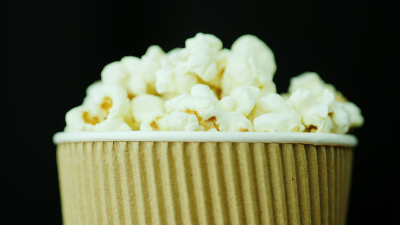 군침 도는 팝콘 한 잔이 영화를 보기 위해 검은색 배경 음식에 대해 부드럽게 회전합니다.